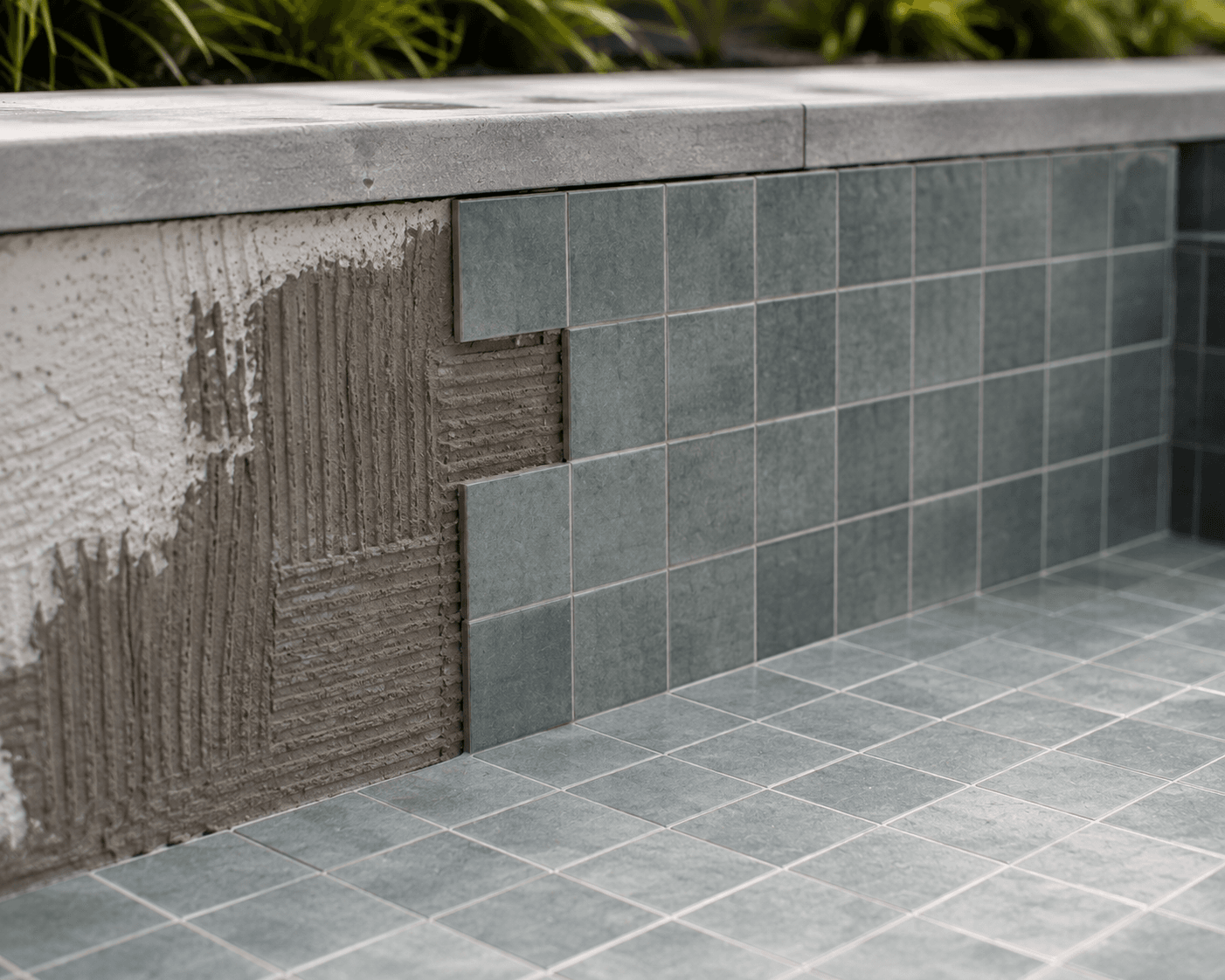 Close-up of concrete pool interior showing tiled step and bench seat with dark grey mosaic tiles and white grout.